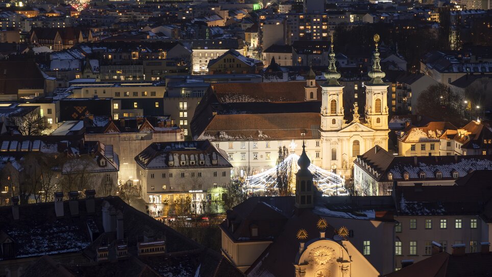 Illuminated city of Graz at night with snow on rooftops and Mariahilferplatz in the foreground. | © Vincent Croce