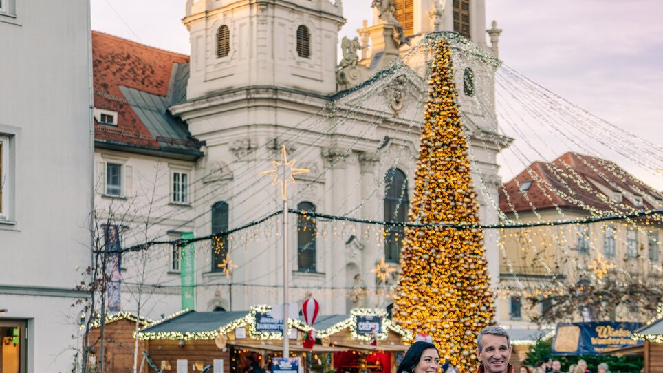 A couple walks on Mariahilferplatz in Graz, surrounded by lights and a Christmas tree. | © Graz Tourismus - Mias Photoart