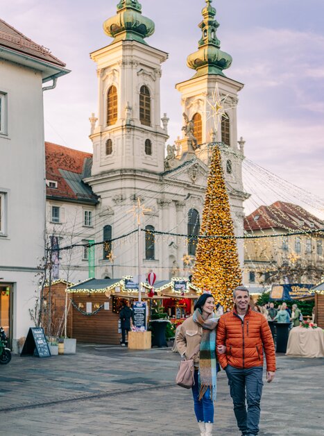 A couple walks on Mariahilferplatz in Graz, surrounded by lights and a Christmas tree. | © Graz Tourismus - Mias Photoart