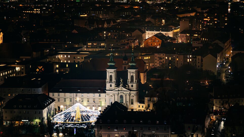 Illuminated Christmas market in Graz at night, with the church in the background. | © Graz Tourismus - Mias Photoart