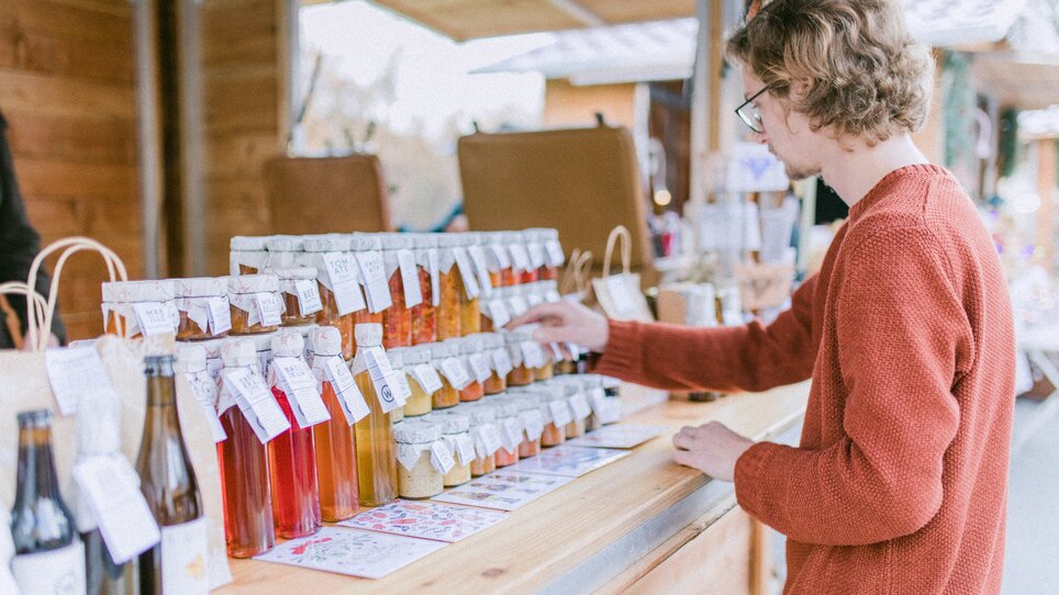 Ein junger Mann betrachtet eine Auswahl von Flaschen mit verschiedenen Inhalten auf einem Weihnachtsmarkt. | © Evgenia Rieger Photography
