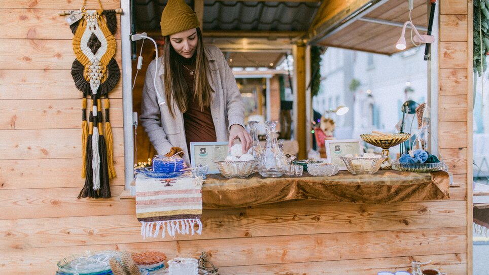 Eine Frau steht an einem Marktstand und verkauft Geschirr und Dekorationsartikel. | © Evgenia Rieger Photography