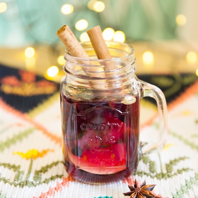 A glass of punch, garnished with cinnamon sticks and star anise, with atmospheric lights in the background. | © Evgenia Rieger Photography