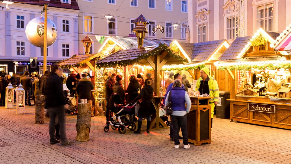 Busy scene at the Christmas market in Graz with festively decorated wooden stalls and visitors. | © Graz Tourismus - Harry Schiffer