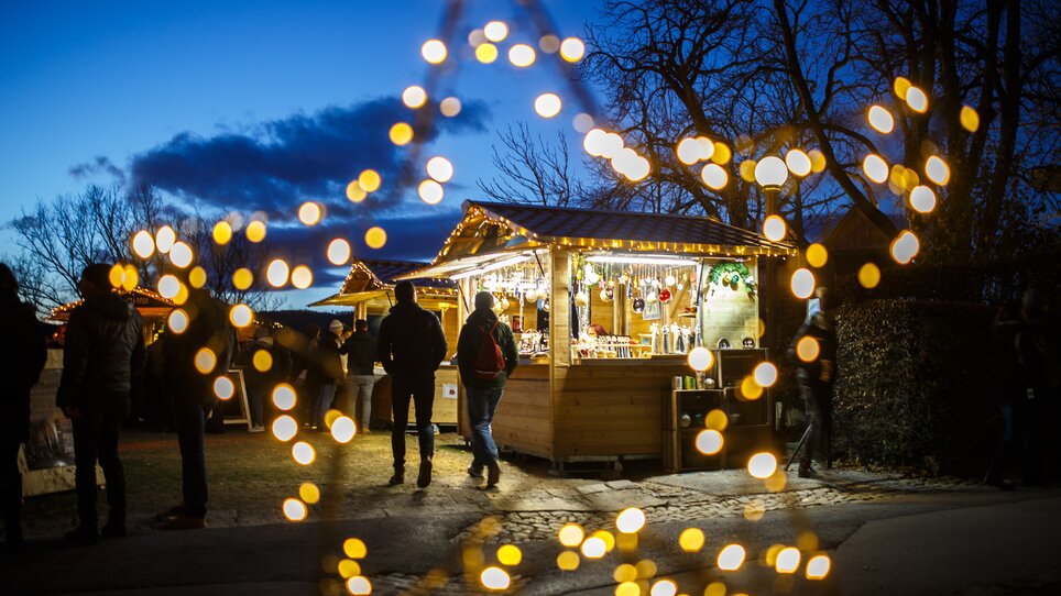 Weihnachtsmarkt mit bunten Lichtern und Ständen, unter blauem Himmel. | © ivents - Erwin Scheriau