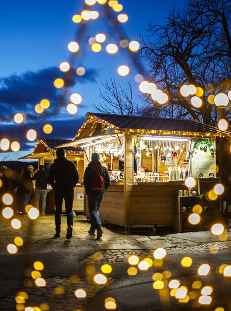 Mercatino di Natale con luci colorate e stand sotto un cielo blu. | © ivents - Erwin Scheriau