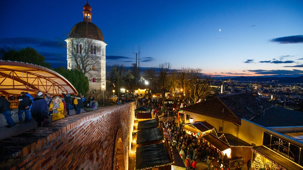 Blick auf den Grazer Glockenturm, Weihnachtsmarktstände und die Stadt Graz im Abendlicht. | © ivents - Erwin Scheriau