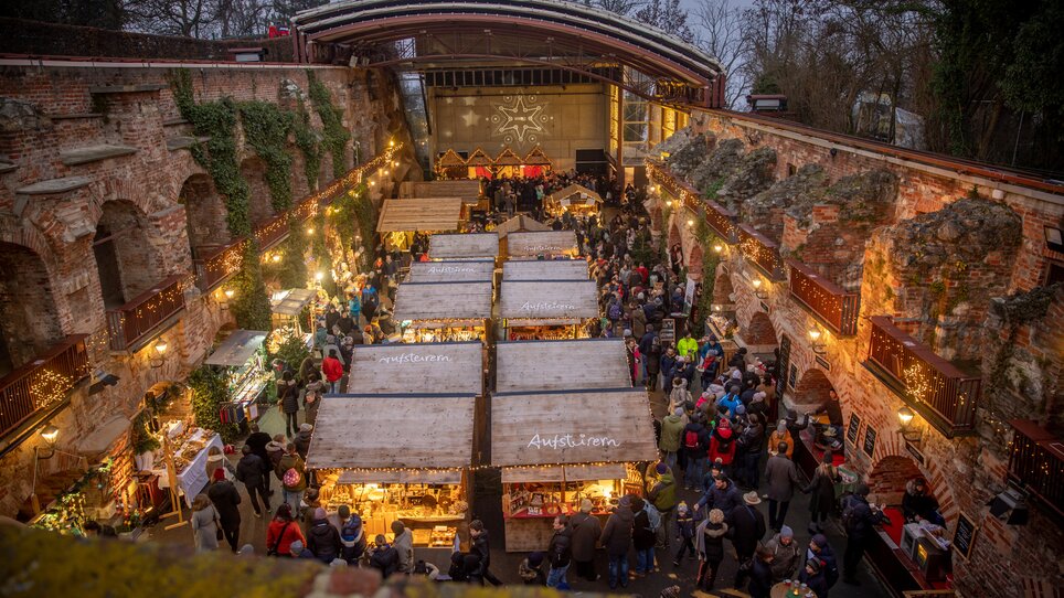 Der Weihnachtsmarkt auf dem Schlossberg in Graz, mit stimmungsvoller Beleuchtung und vielen Besuchern, die die Stände erkunden. | © ivents