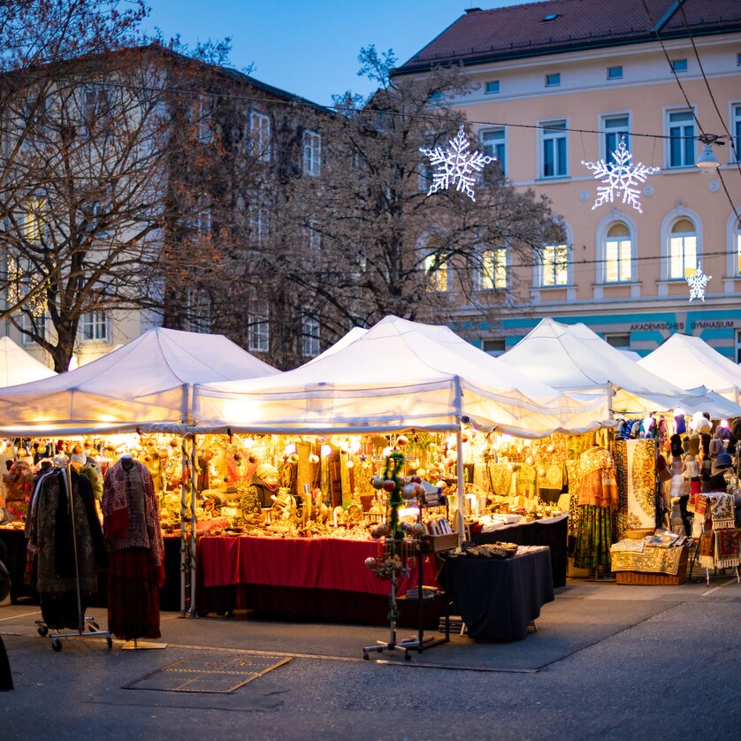 A festive Advent market scene with brightly lit stalls and people in Graz. | © Graz Tourismus - Harry Schiffer