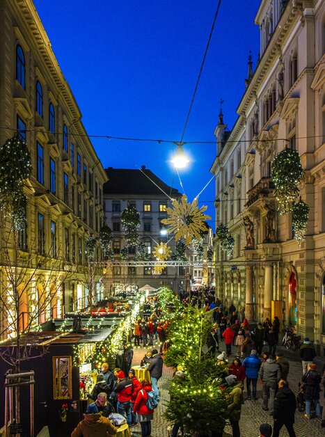 Beleuchtete Adventstände und Weihnachtsmarkt in der Schmiedgasse, Graz, festlicher Abend mit vielen Besuchern. | © Rene Walter