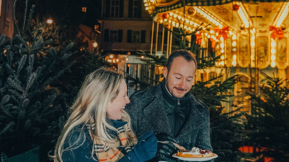 A couple enjoys the Christmas atmosphere at Karmeliterplatz in Graz with a carousel in the background. | © Mias Photoart