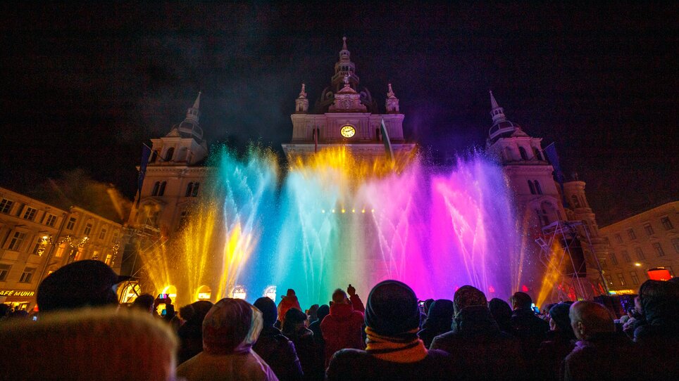 Persone guardano uno spettacolo d'acqua e luce colorato nella piazza principale di Graz. | © Ivents-Kulturagentur - Erwin Scheriau