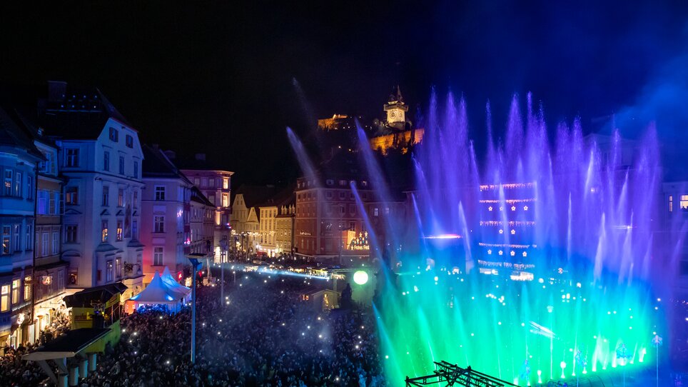 Fontane illuminate a Graz durante lo spettacolo di Capodanno, sullo sfondo la Torre dell'Orologio di Graz. | © Ivents-Kulturagentur - Erwin Scheriau