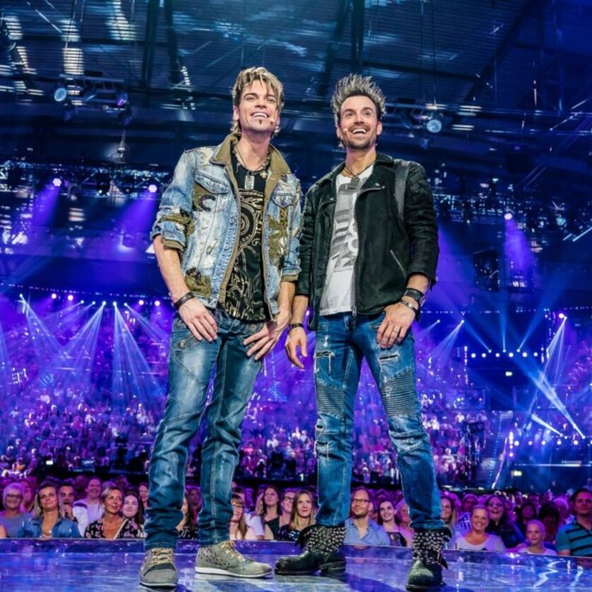 The magigians EHRLICH BROTHERS are standing on a stage, wearing jeans, colorful T-Shirts and sporty jackets | © Ralph Larmann Gross