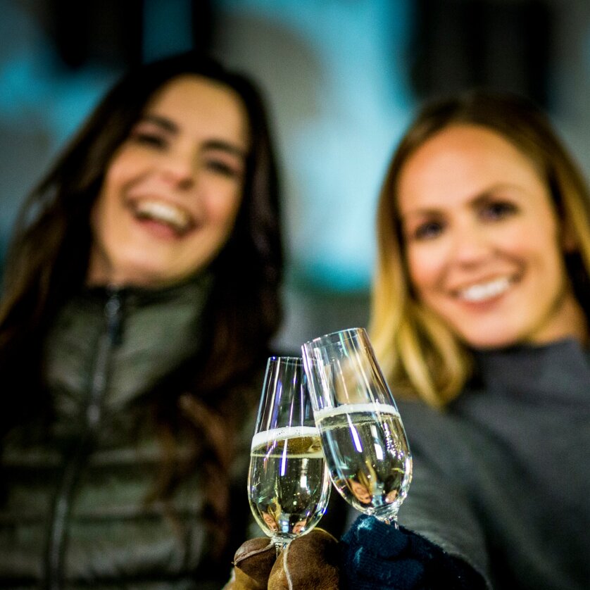 Advent in Graz I Winter in der Steiermark | © Graz Tourismus - Tom Lamm Zwei Frauen halten Sektgläser in der Nacht und lächeln. | © Graz Tourismus - Tom Lamm