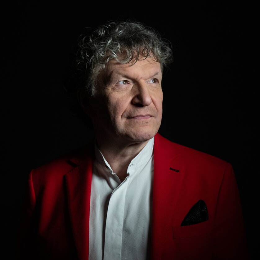 A man with curly hair in a red blazer, facing forward, illuminated against a dark background. | © Christian_Jungwirth_verk