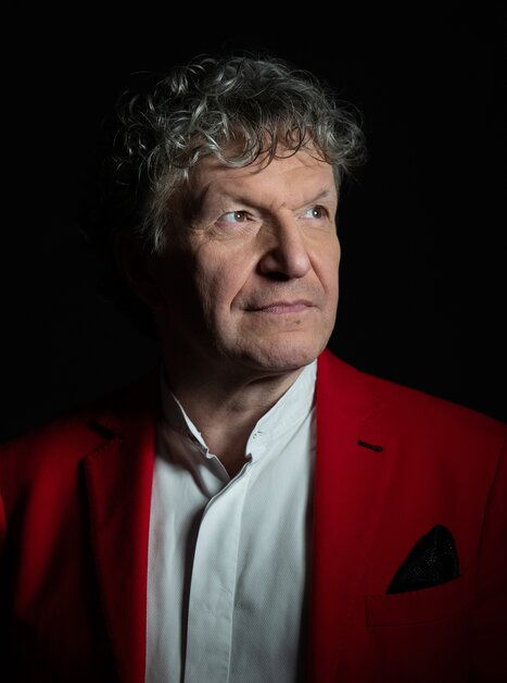 A man with curly hair in a red blazer, facing forward, illuminated against a dark background. | © Christian_Jungwirth_verk