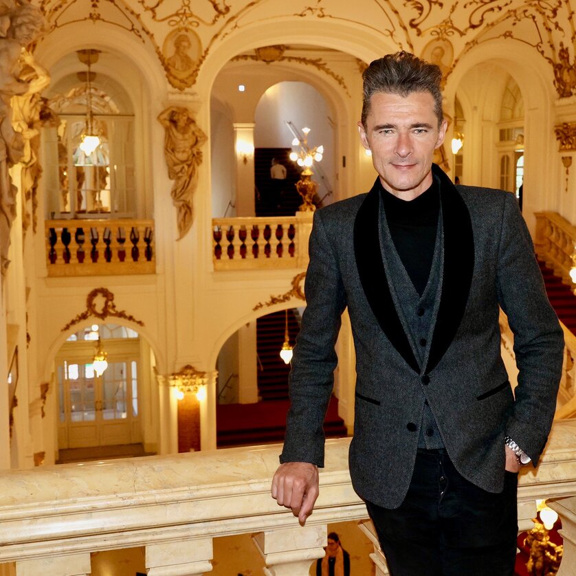 © Ivents Kulturagentur Herbert Pixner leans against the balcony railing of the Graz Opera House, behind him you can see the staircase with the red carpet. | © Ivents Kulturagentur