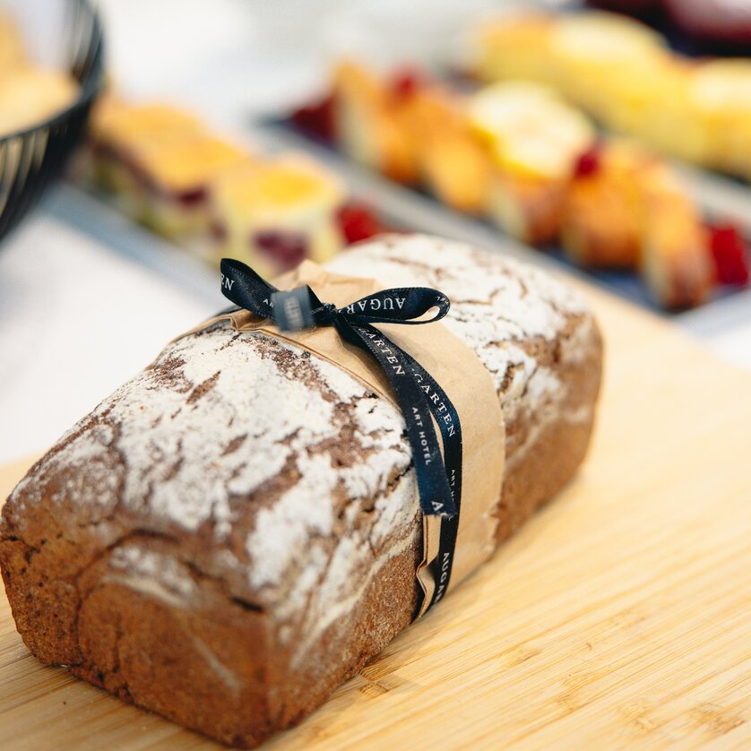 A loaf of brown bread decorated with a bow and the Augarten Art Hotel logo | © Augartenhotel x einsnullneun