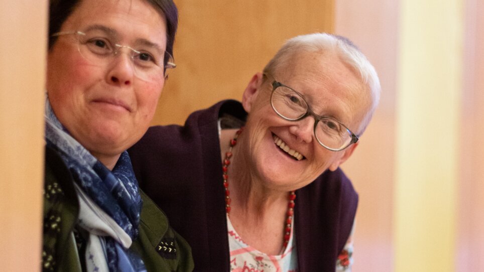 Zwei bunt gekleidete Frauen mit kurzen Haaren, die ältere von ihnen lächelt vergnügt in die Kamera. | © Péter Grátz