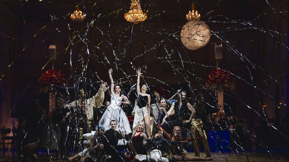 Tanzende Künstler in Festkleidung vor einem festlichen Hintergrund.