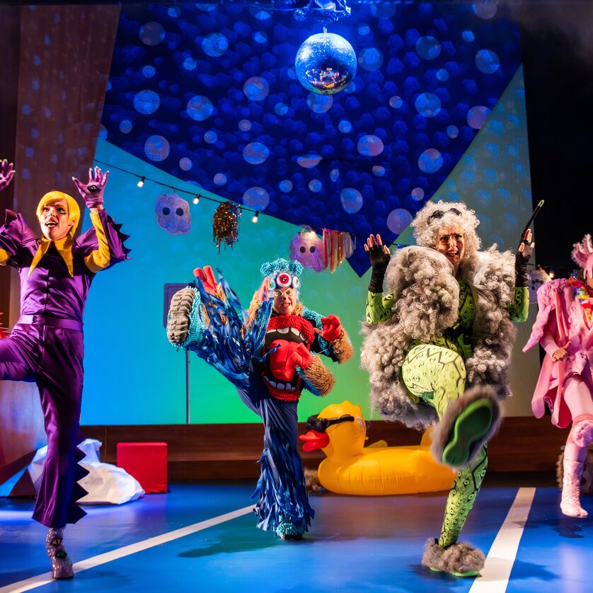 Fünf Personen in bunten Kostümen tanzen fröhlich auf der Bühne.