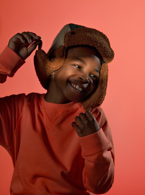 Ein fröhliches Kind in Orange trägt eine Plüschmütze und lächelt. | © Stella