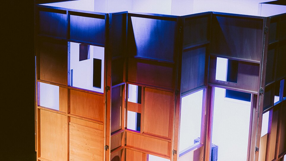 Zwei Darsteller sitzen vor einer beleuchteten Holzstruktur auf der Bühne. | © Stella