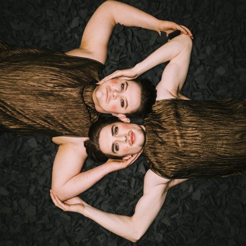 Two persons in bronze outfits lying on black material. | © Oper Graz - Ingo-Pertramer