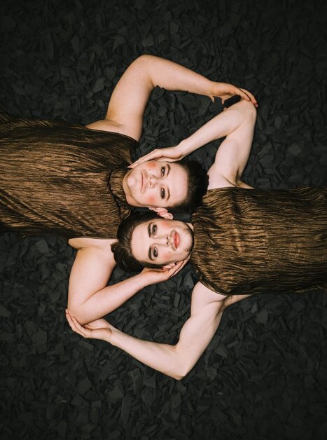 Two persons in bronze outfits lying on black material. | © Oper Graz - Ingo-Pertramer
