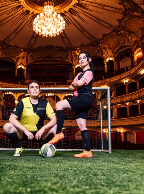 Zwei Künstler:innen im Fußballtrikot posieren in einem prächtigen Theater mit Fußballtor. | © Ingo Pertramer - Oper Graz