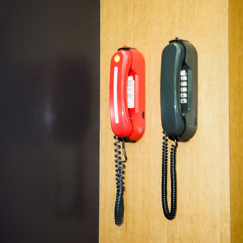 Zwei Telefonhörer, einer rot und einer schwarz, hängen an einer Wand. | © Antonia Harborth