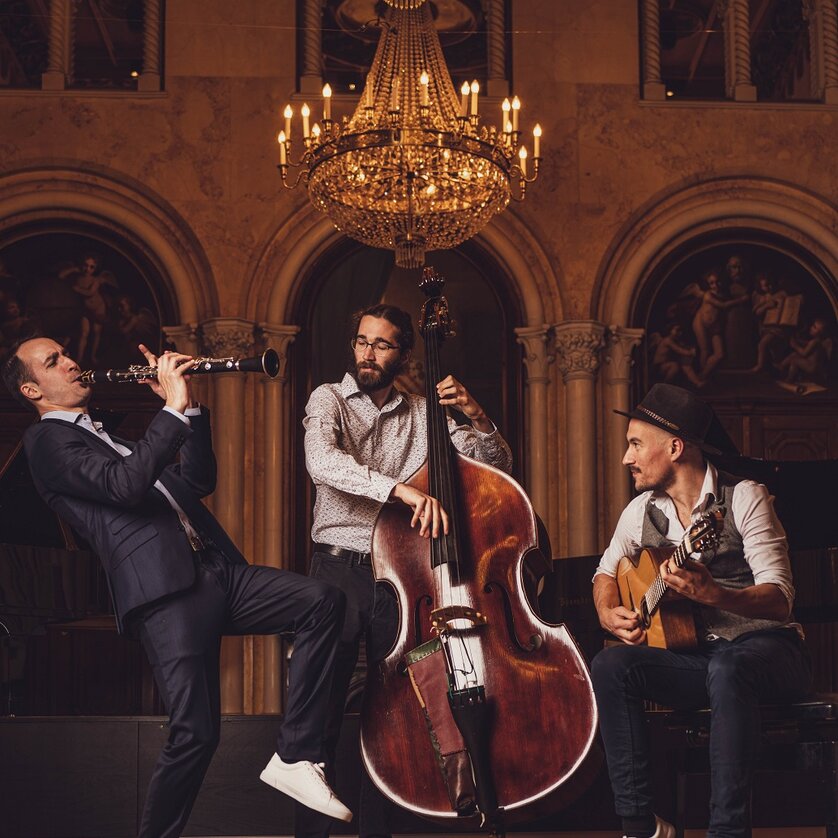 Drei Musiker spielen in einem prunkvollen Raum: Klarinette, Kontrabass und Gitarre. | © reithofer-media.com