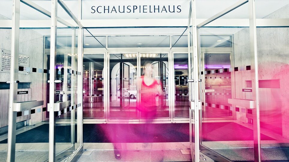 Una persona entra nello Schauspielhaus attraverso porte girevoli in vetro. | © Lupi Spuma
