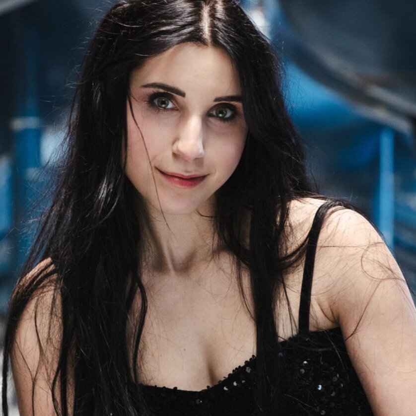 Anna-Sophie | © Zoe Goldstein Woman with long dark hair wearing a black top, posing in a modern blue environment. | © Zoe Goldstein