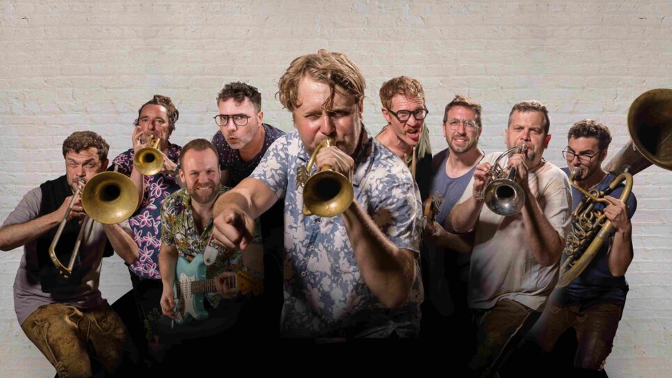 A group of musicians with trumpets and a guitar pose energetically for the photo. | © David Königsmann