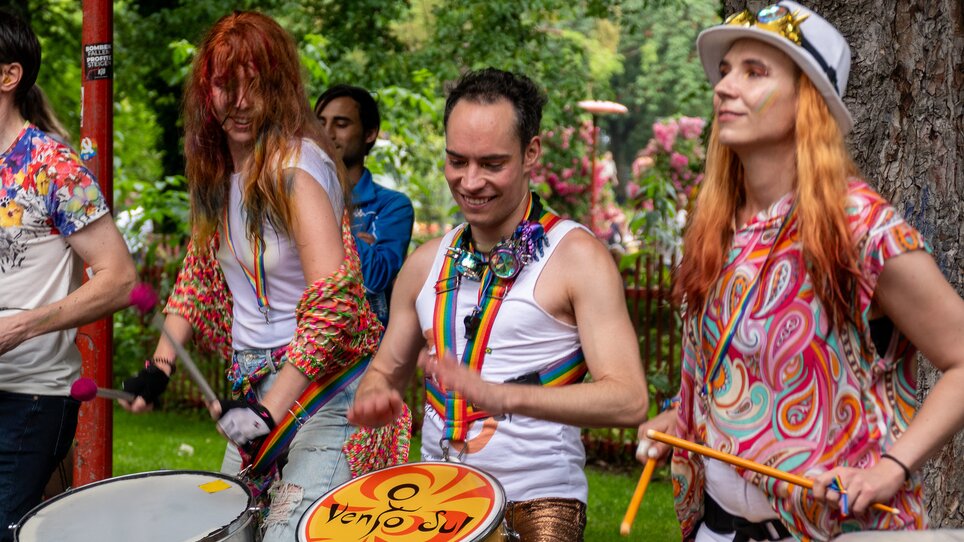 Bunte Musikgruppe mit Trommeln und Kleidung in Regenbogenfarben. | © Maya Hanl