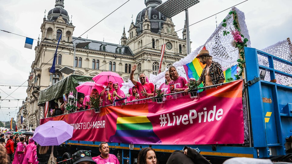 Teilnehmer des CSD Graz mit Regenbogenfahnen und pinken Regenschirmen auf einem Wagen. | © Sebastian Neugebauer
