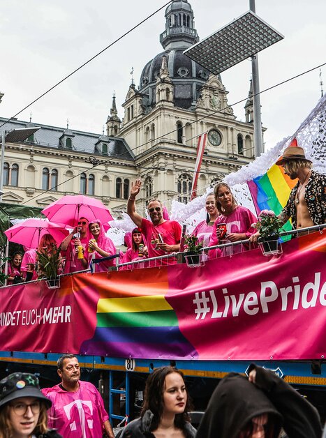 Teilnehmer des CSD Graz mit Regenbogenfahnen und pinken Regenschirmen auf einem Wagen. | © Sebastian Neugebauer
