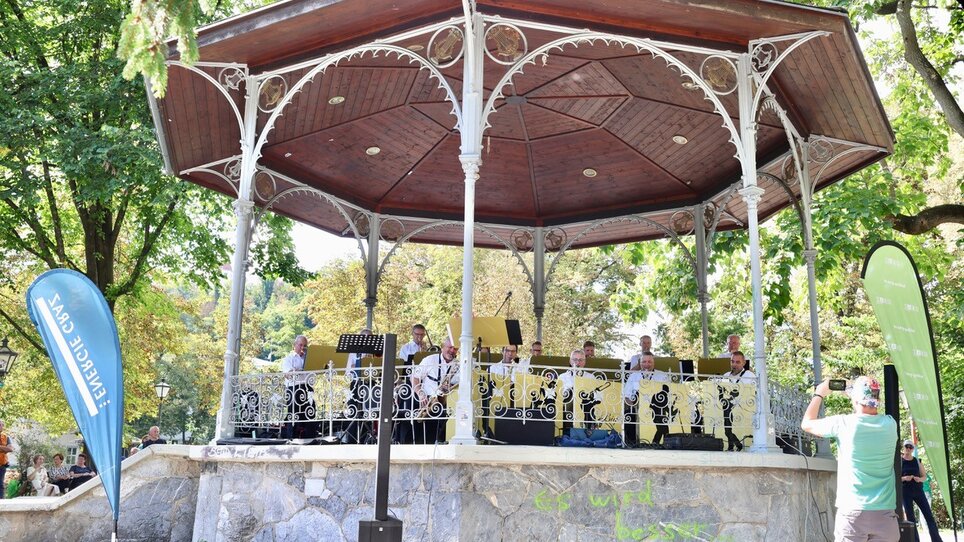 Brass band performs outdoors, surrounded by trees. | © Sandra Danzer