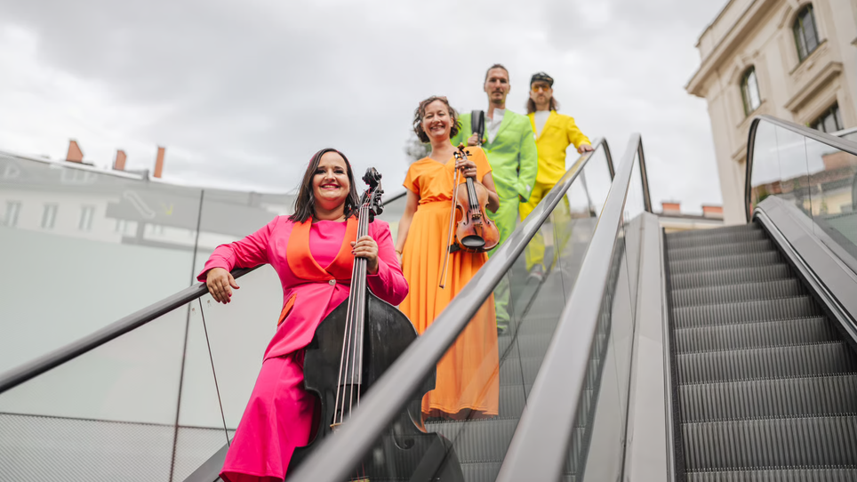 Four musicians in colorful outfits, one with a cello, posing on a staircase. | © Simon Reithofer