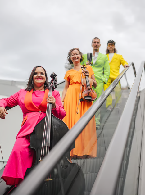 Four musicians in colorful outfits, one with a cello, posing on a staircase. | © Simon Reithofer