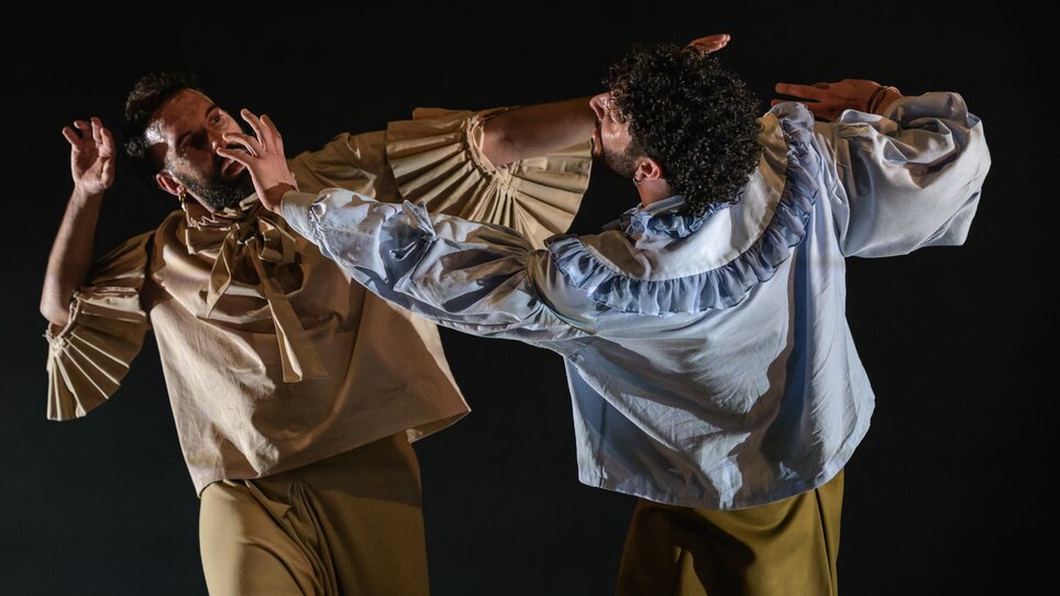 Due danzatori in abbigliamento elegante interagiscono in modo potente sul palco. | © Int. Bühnenwerkstatt