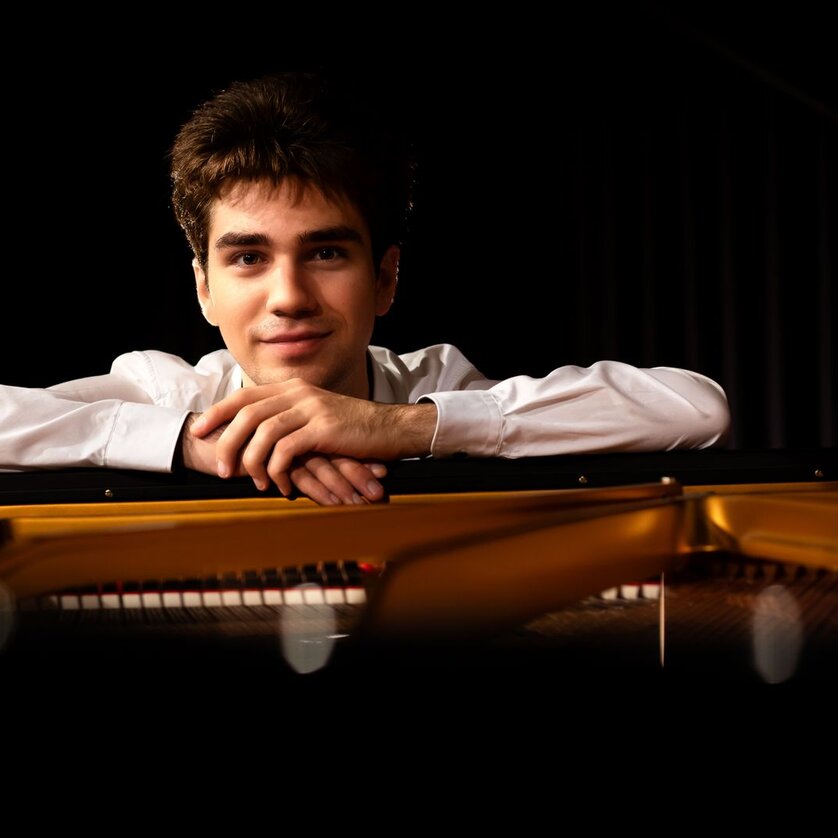 Ein junger Mann lehnt an einem Klavier und lächelt. | © Christoph Preiss
