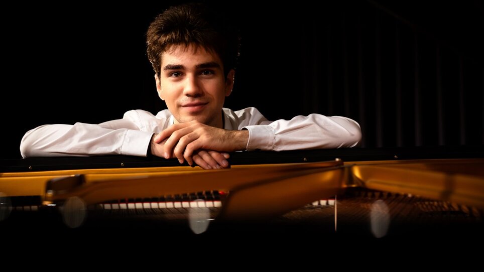 Ein junger Mann lehnt an einem Klavier und lächelt. | © Christoph Preiss