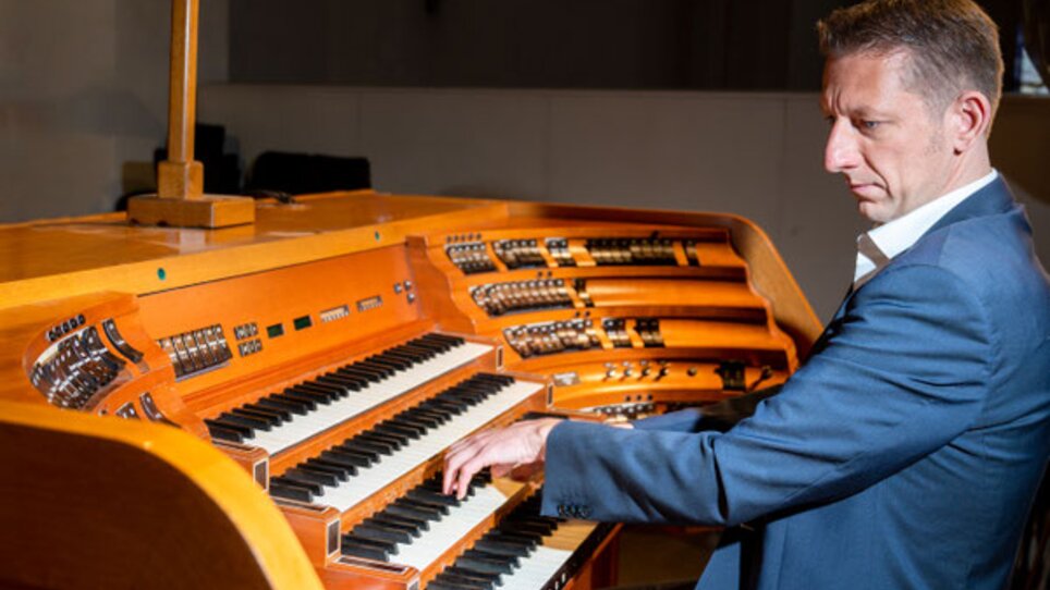 Ein Mann in einem Anzug spielt an einer Orgel mit Holzoberfläche. | © Sandra Wolf