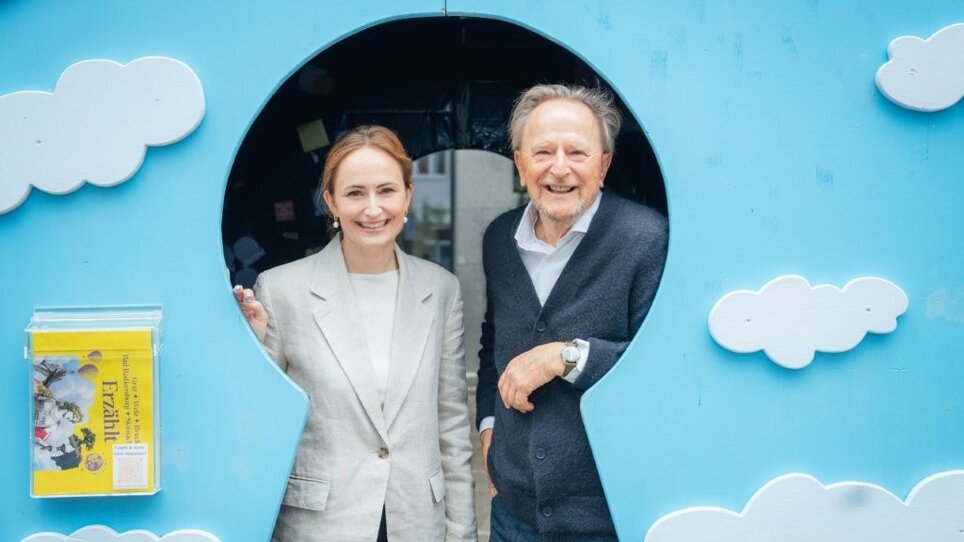 Tessa Erker-Tegetthoff e Folke Tegetthoff  sono in piedi sotto l'arco d'ingresso di un castello da favola blu con nuvole bianche. | © Florian Matzi