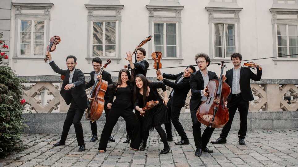 An ensemble in elegant outfits poses energetically outdoors. | © Marija Jancic