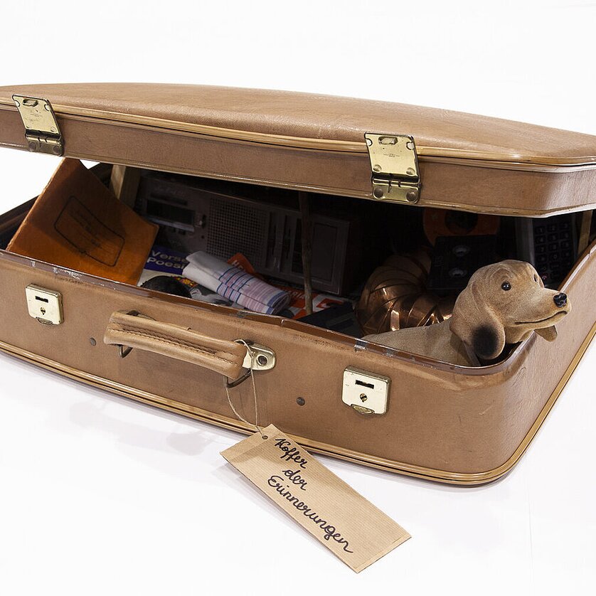 Ein geöffneter Koffer voller Gegenstände und einer Hundefigur. | © Magdalena Gföllner