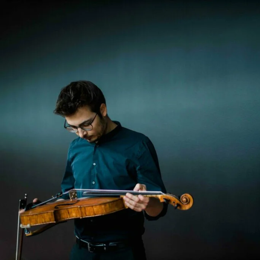 Ein Musiker schaut auf seine Geige vor einem dunklen Hintergrund. | © Theresa Pewal